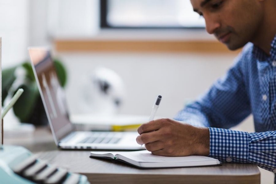 Graduate writing on notebook and researching on laptop