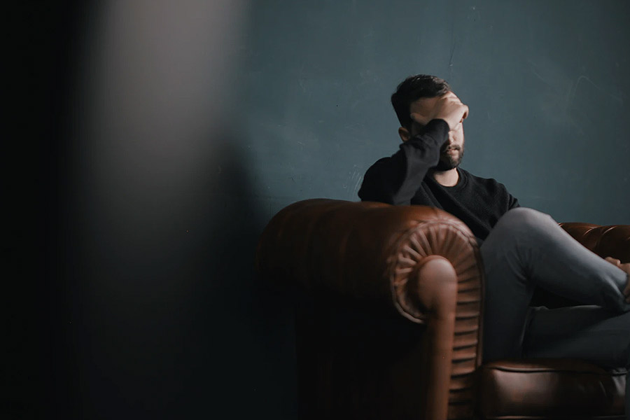 man on a sofa holding head in hand looking depressed