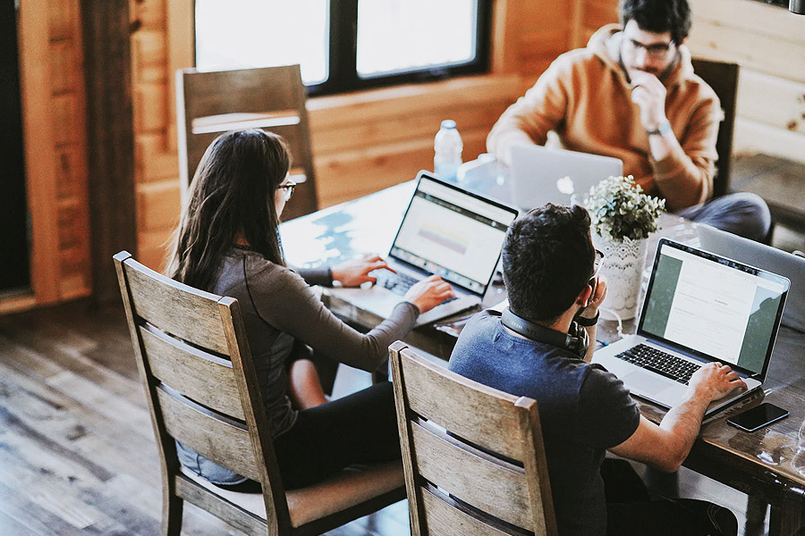 group of students sat round a desk on laptops wokring