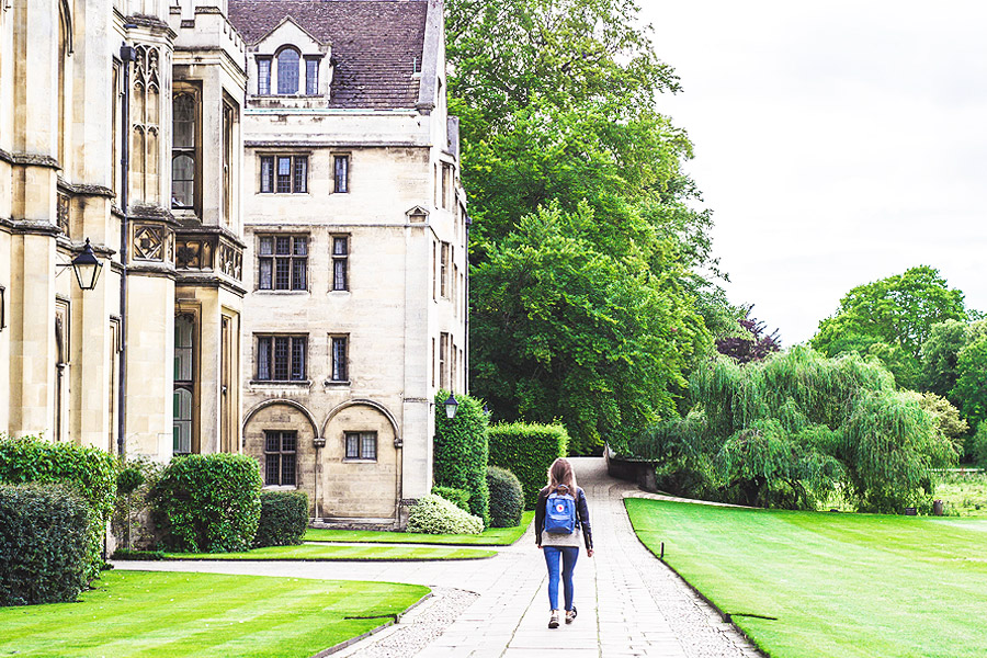 young adult with back pack walking next to old university building