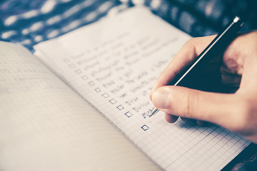 a hand with a pen writing a list on notepad